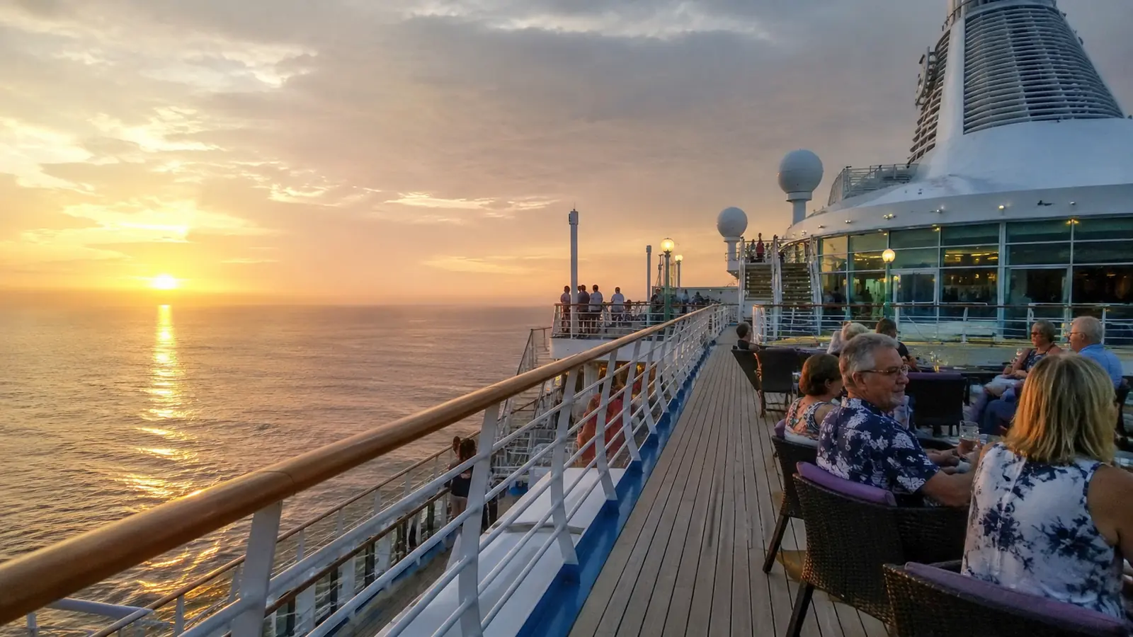 Passengers seated on an outdoor cruise ship deck at sunset