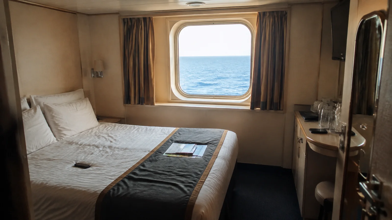 Compact ocean-view cabin with a double bed and desk.