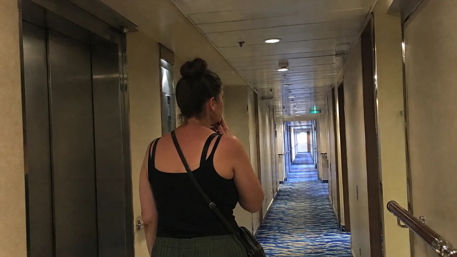 Passenger walking past elevators in a cruise cabin corridor.