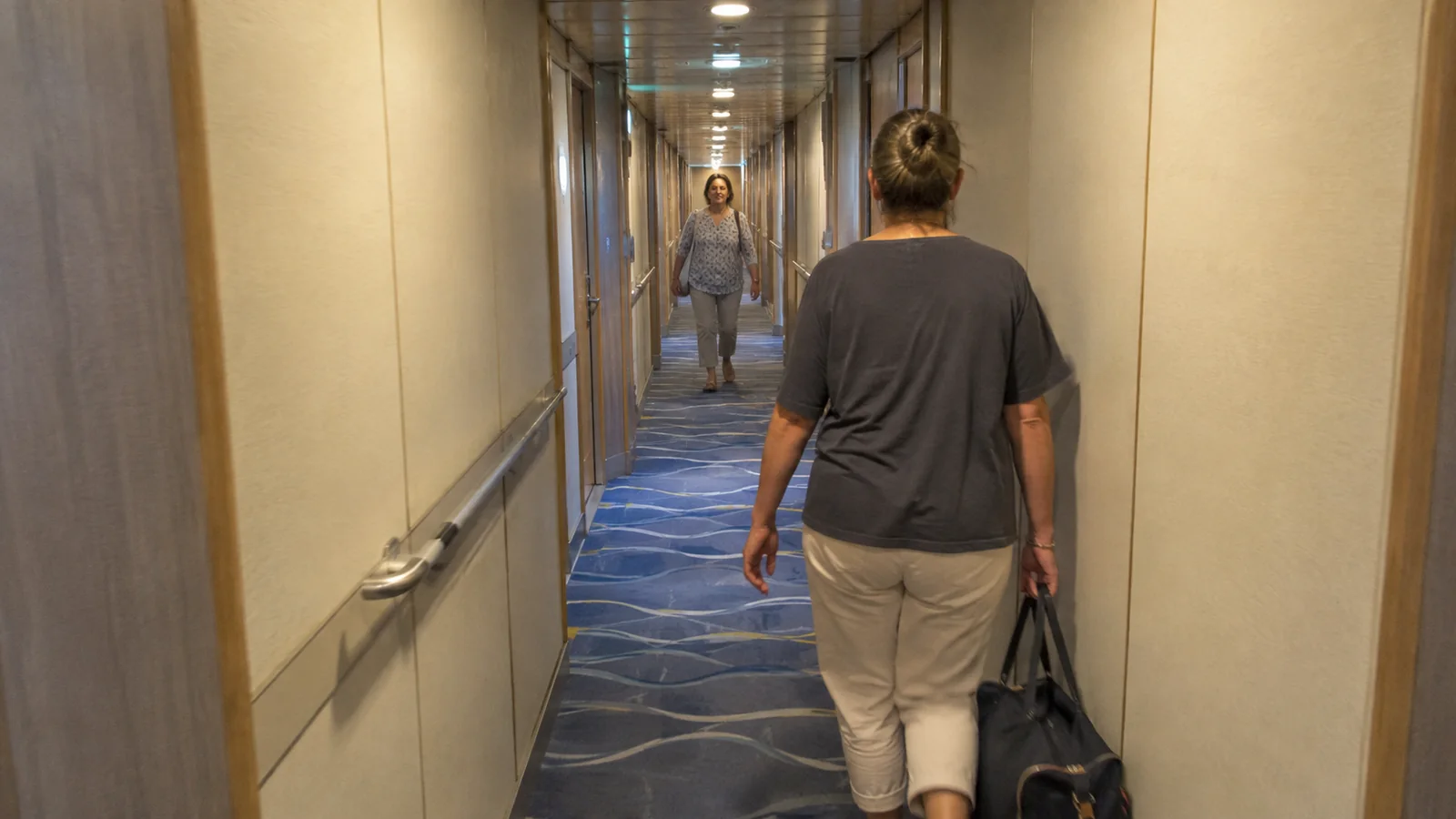 Passenger carrying a bag along a long carpeted hallway.
