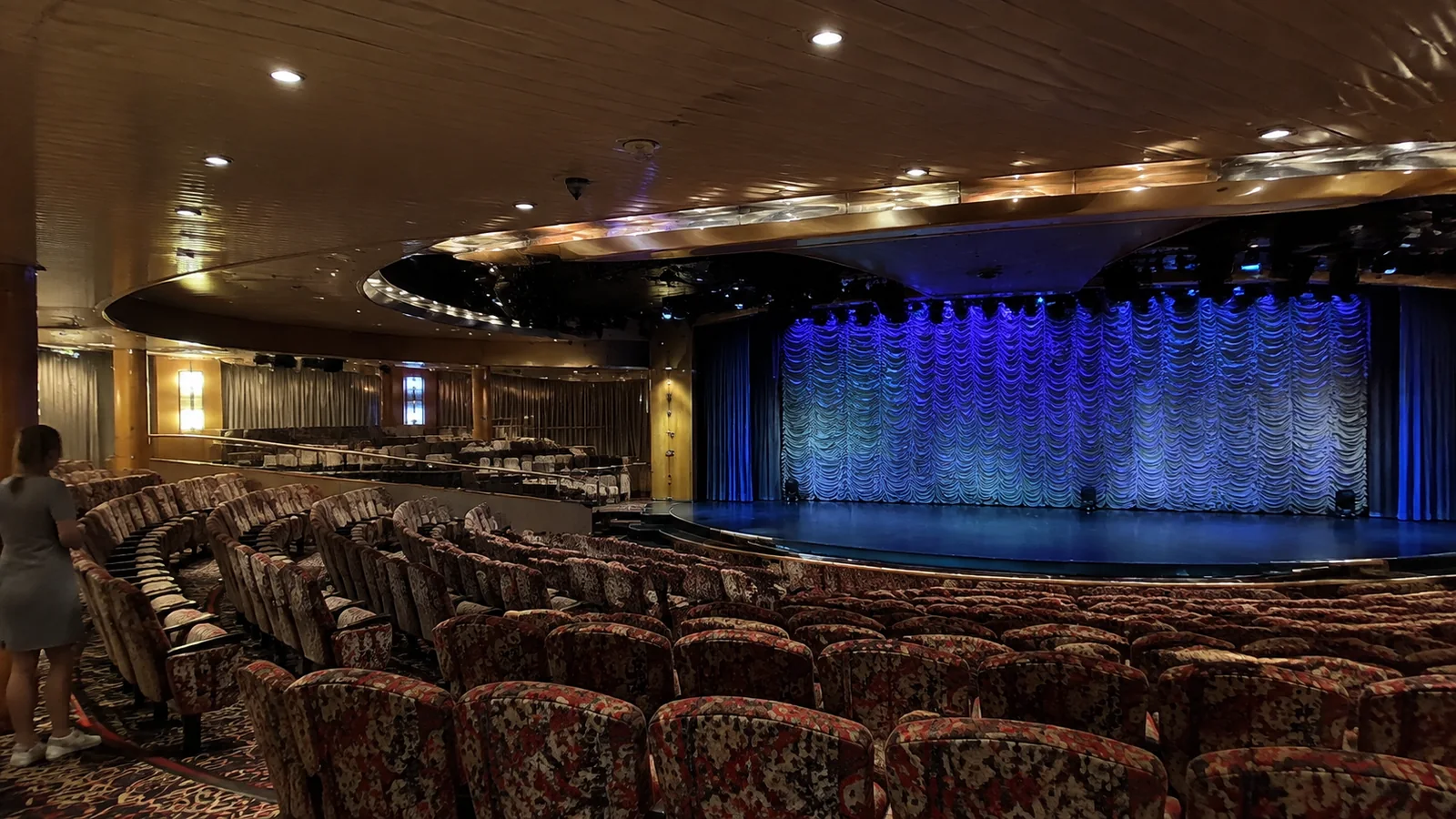 Rows of theater seats face a stage with a blue curtain.