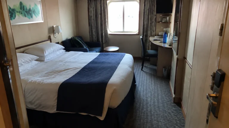 Cruise cabin with a double bed, desk, and curtained window