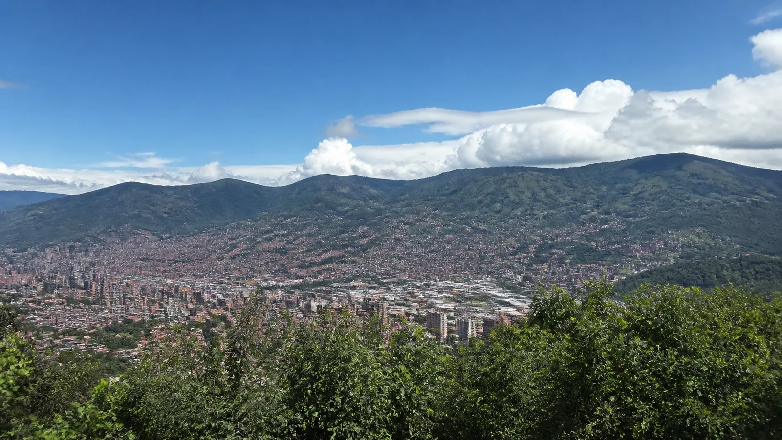 Dense city spreads across a mountain valley beneath blue skies.