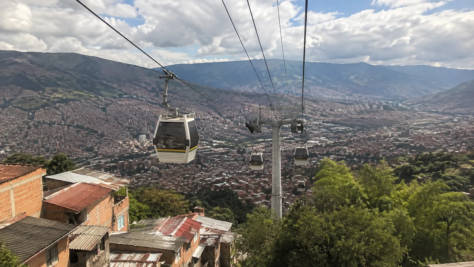 Cable cars suspended above a sprawling hillside city and mountains.