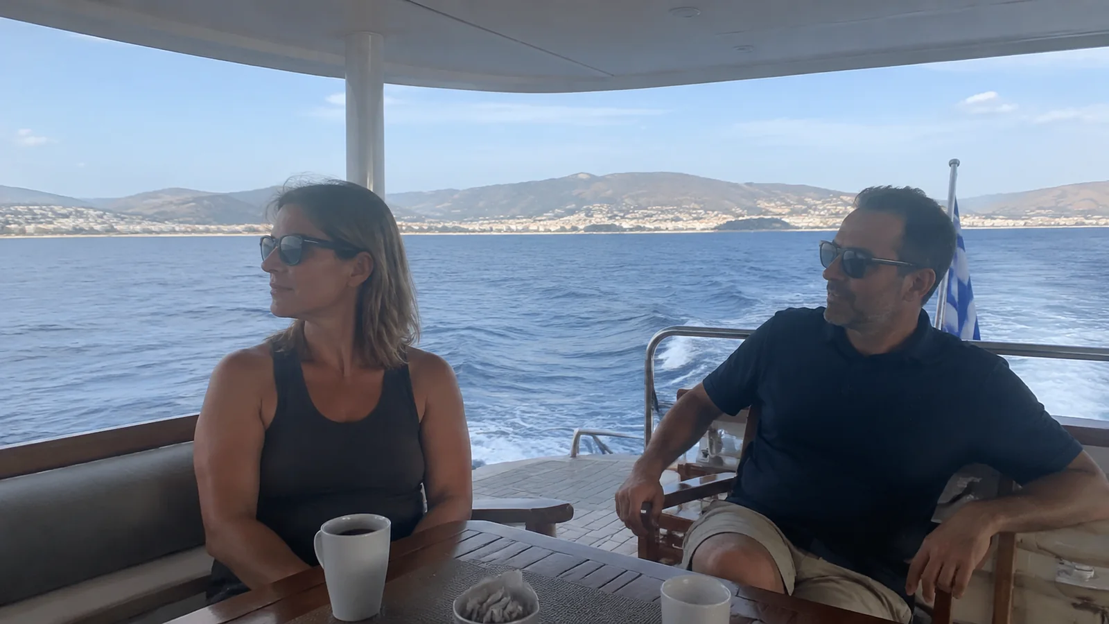 Two passengers relax beneath a canopy on a boat overlooking the sea.