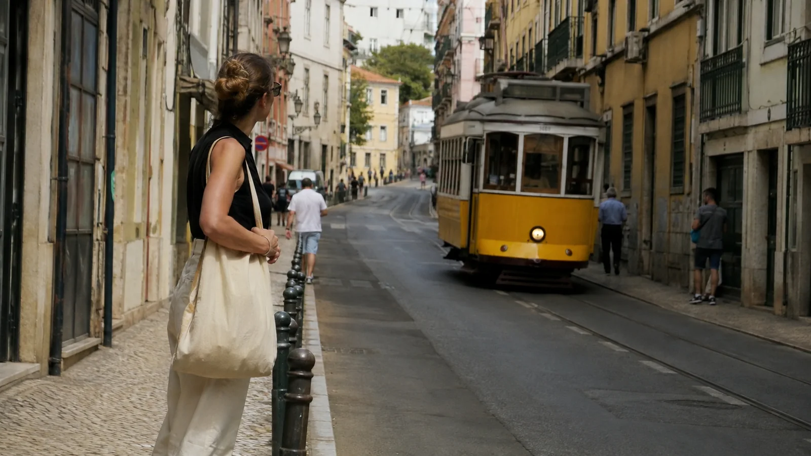 Woman watches a yellow tram pass along a narrow city street.