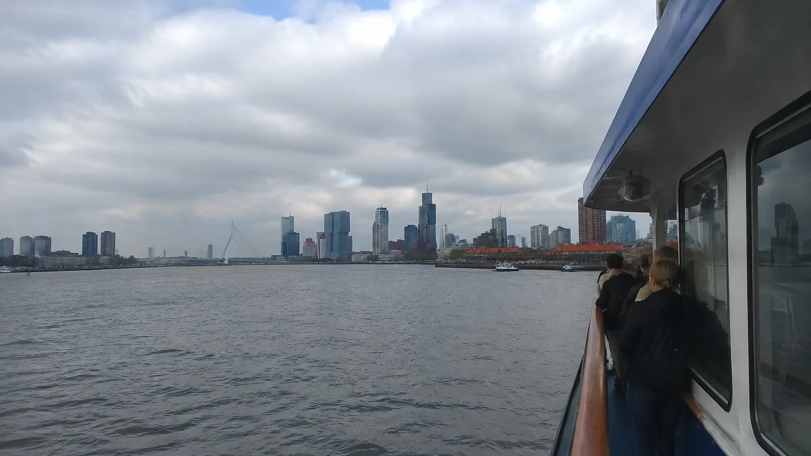 Passengers watching a city skyline from a ship's side deck.