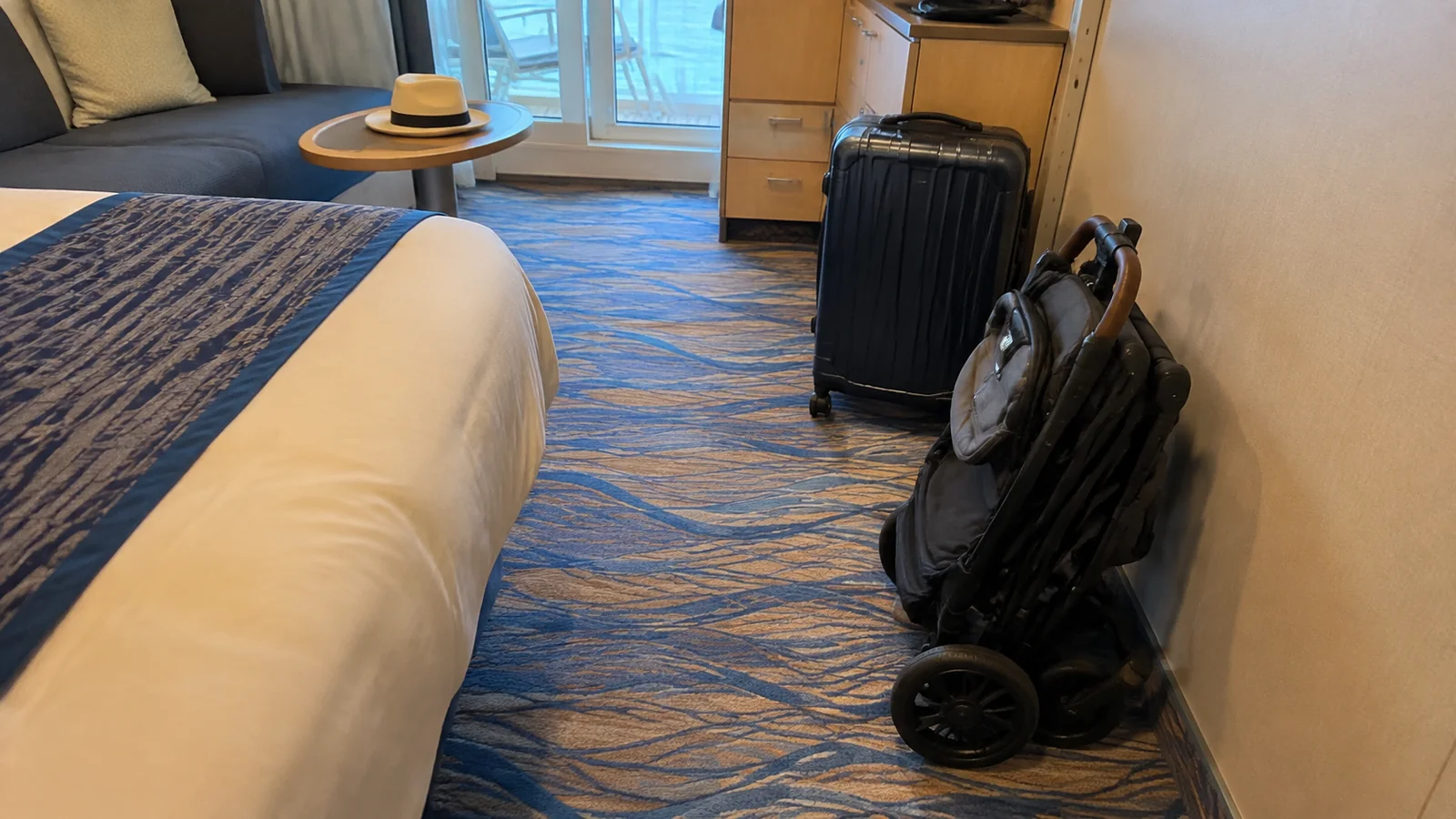 Folded stroller and suitcase beside a bed in a ship cabin.