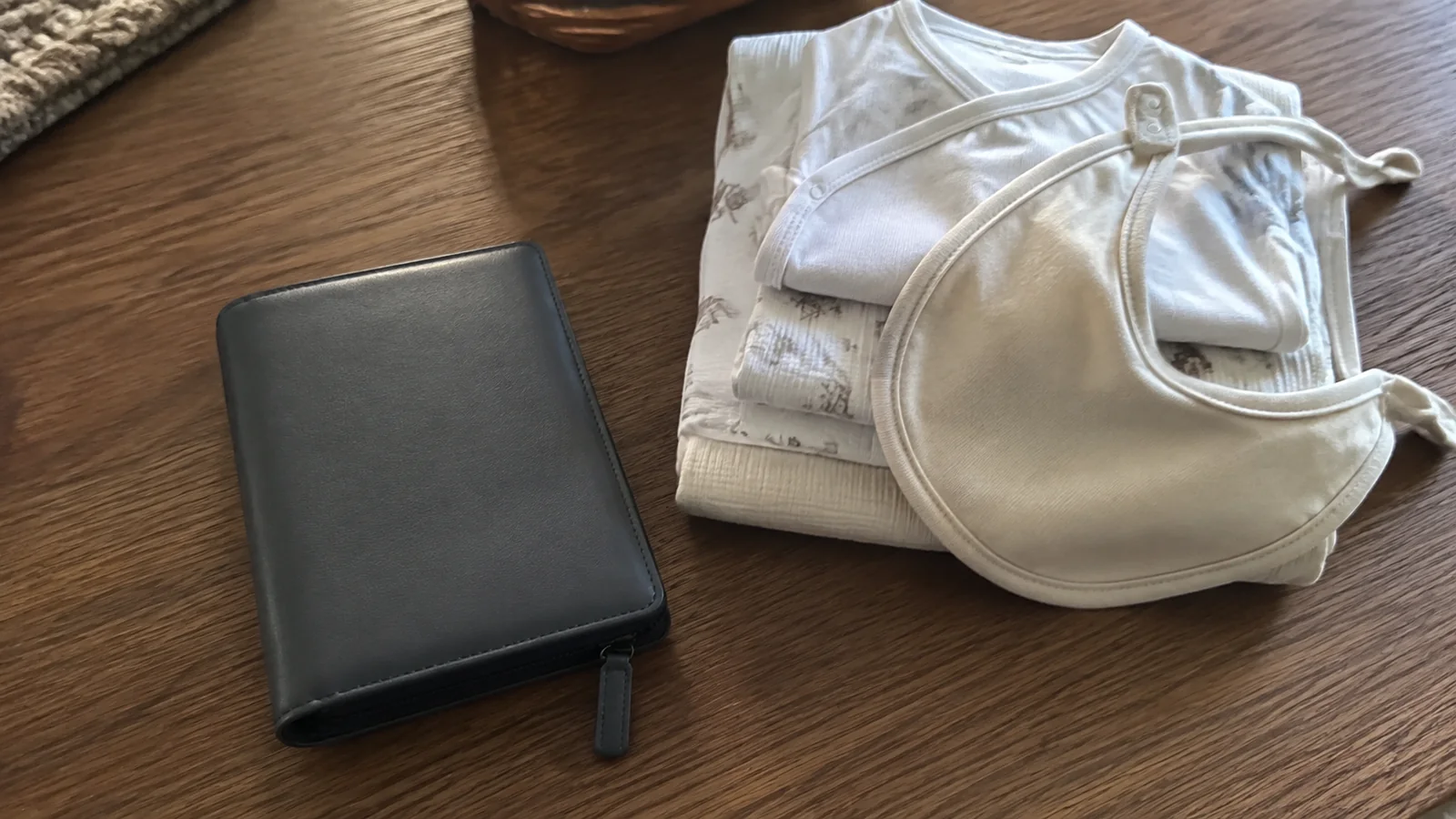 Travel wallet beside neatly folded baby clothing and bibs on a table.