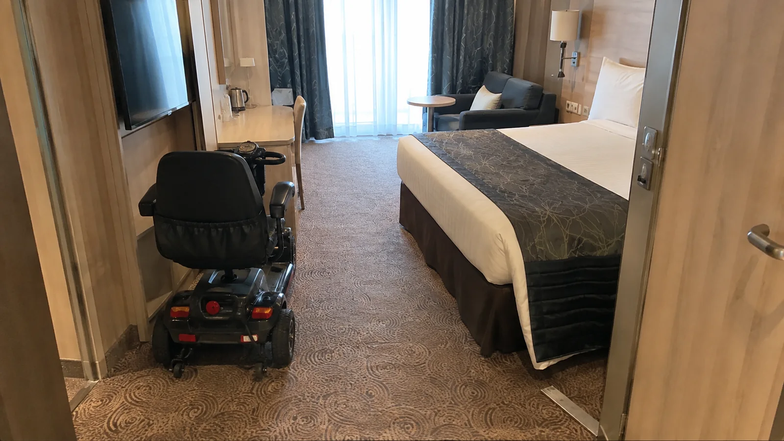 Mobility scooter parked beside a bed inside a spacious ship cabin.