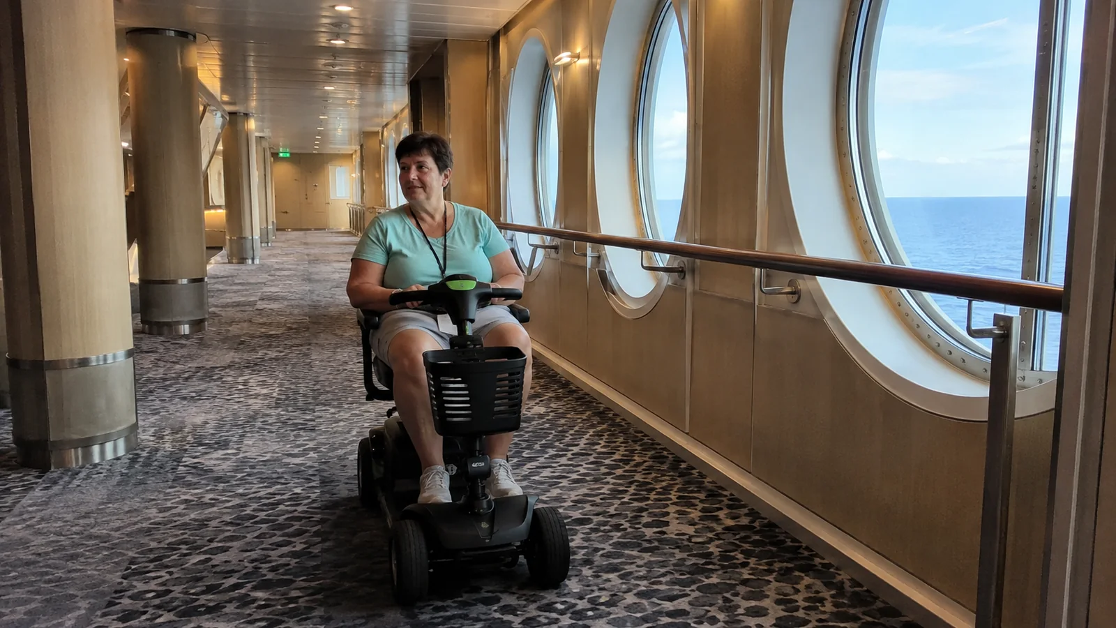 Woman driving a mobility scooter along a wide ship corridor.