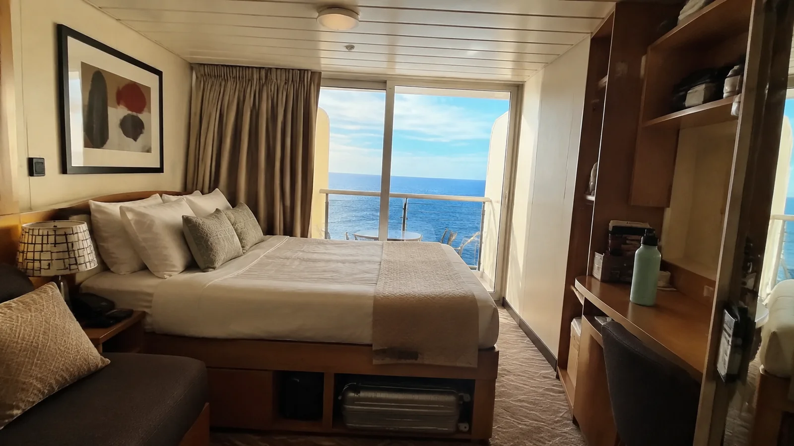 Balcony cabin with a double bed, desk, and ocean view.
