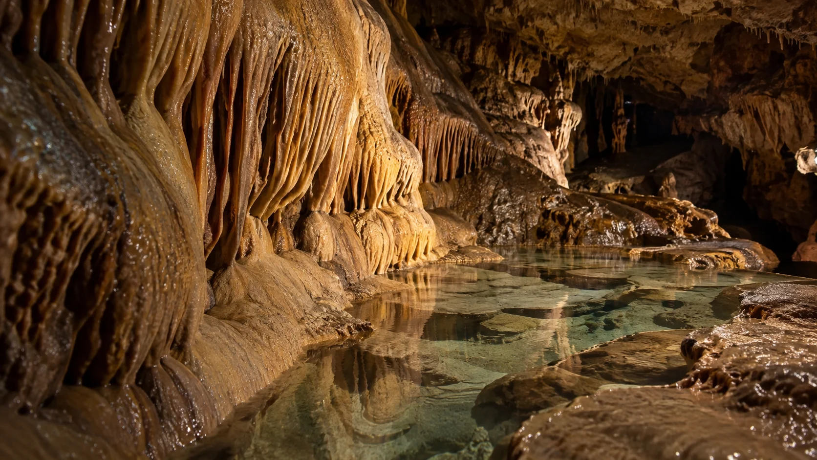 Rippled flowstone curtains hang above a clear shallow pool inside Cave of the Mounds.