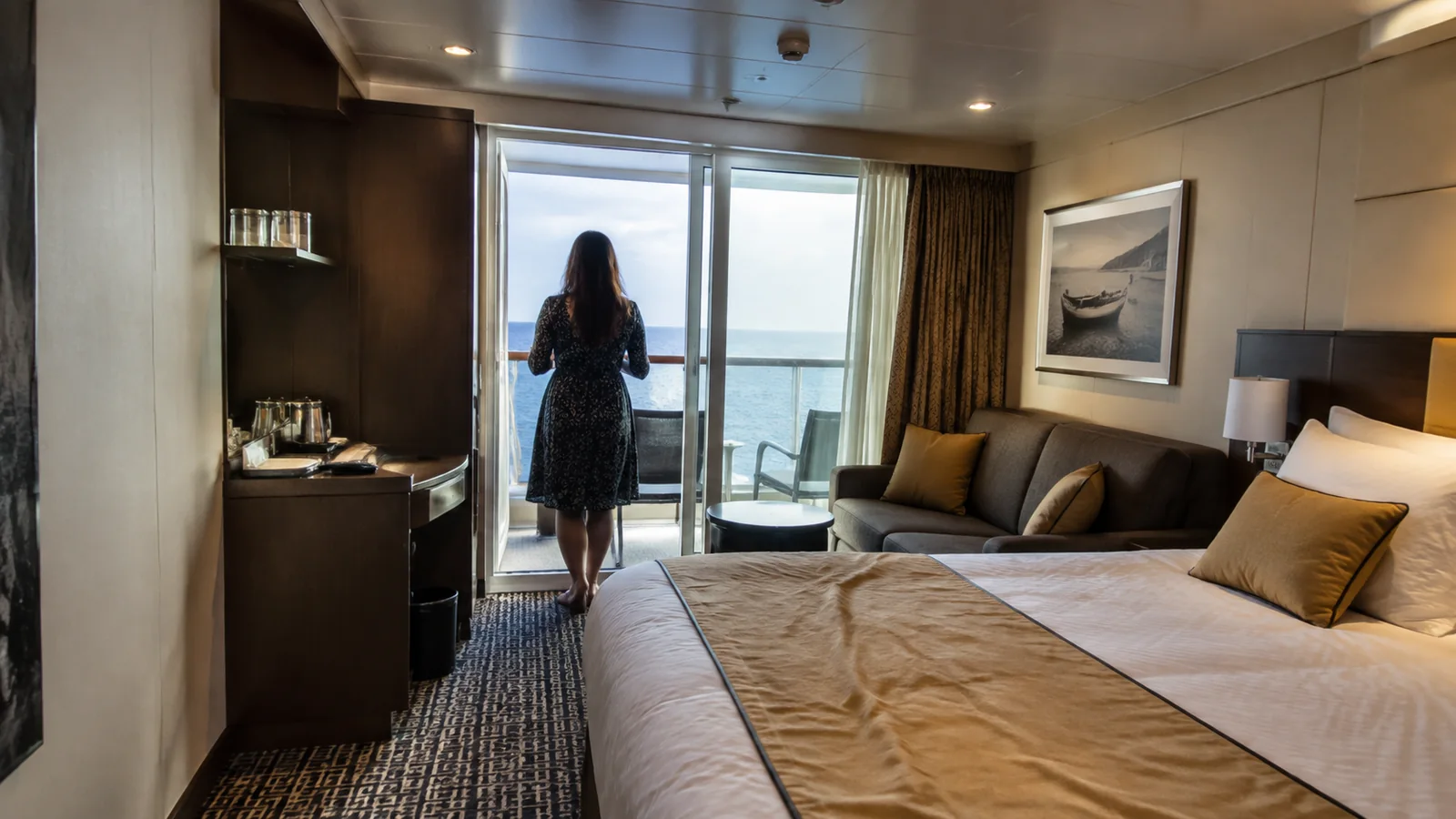 Woman stands at balcony doors in a modern cruise stateroom.