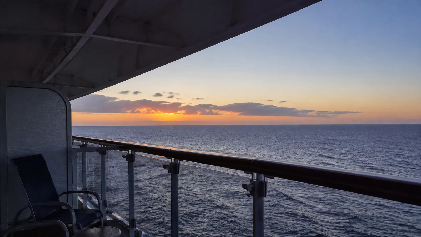 Sunset colors the horizon beyond a sheltered ship balcony.