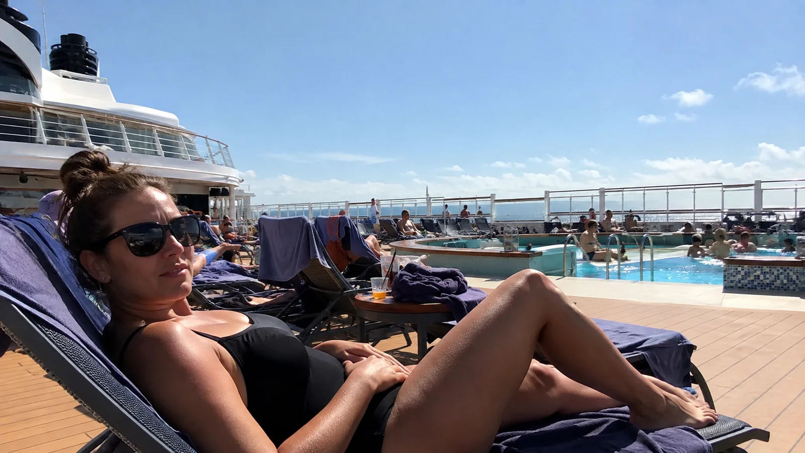 Woman reclines on a lounger beside a busy outdoor pool.