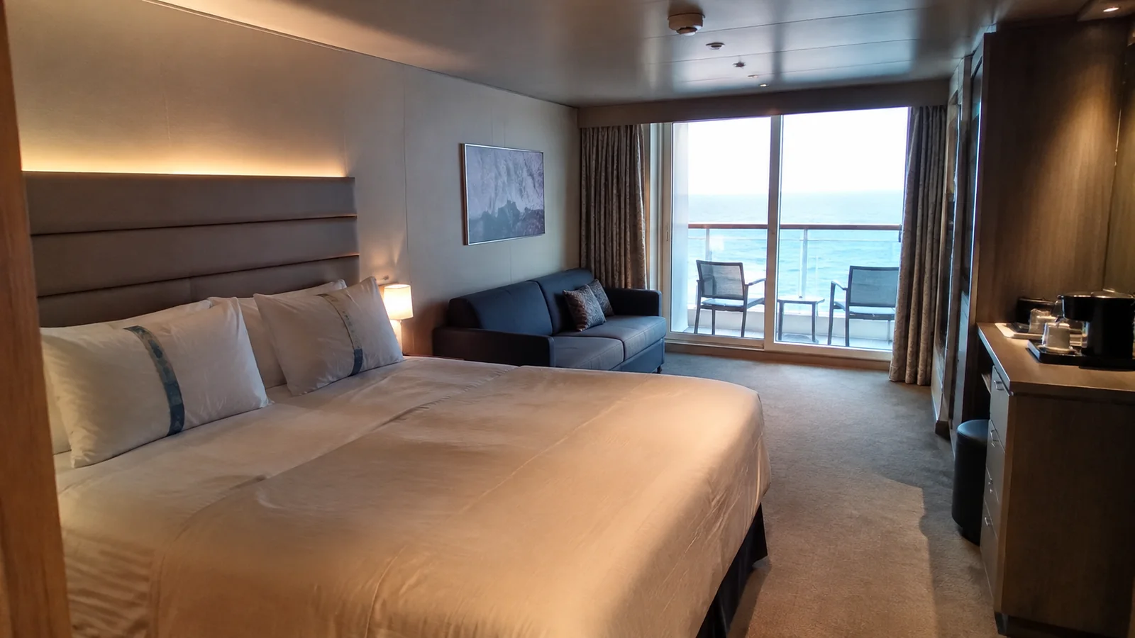 Modern stateroom has a large bed, sofa and ocean balcony.