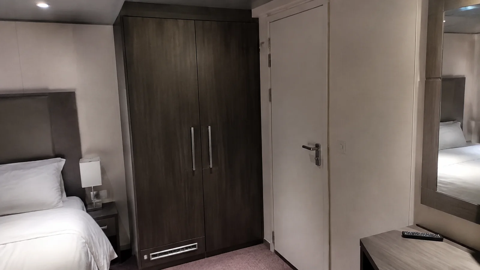 Dark wardrobe and closed pale door stand beside a bed.