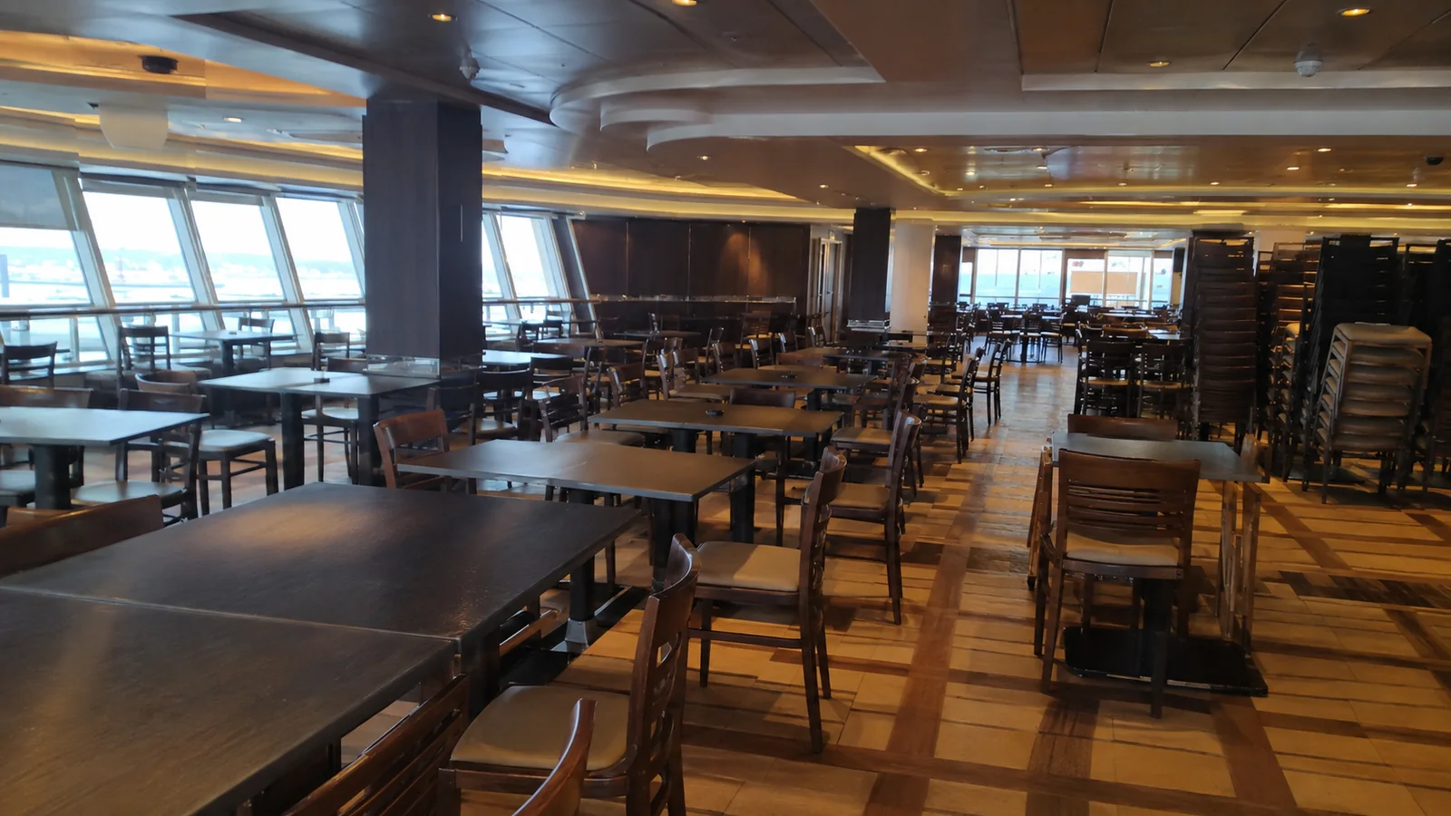 Empty dining tables fill a ship buffet with ocean windows.
