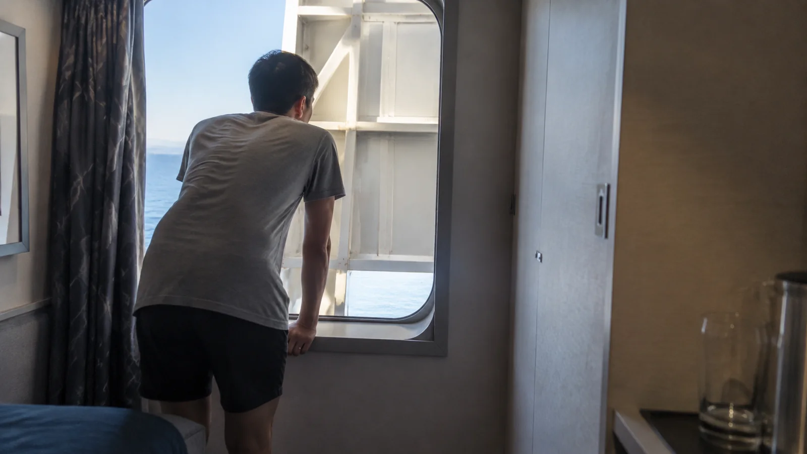 Man looking through a cruise cabin window partly blocked by an exterior structure