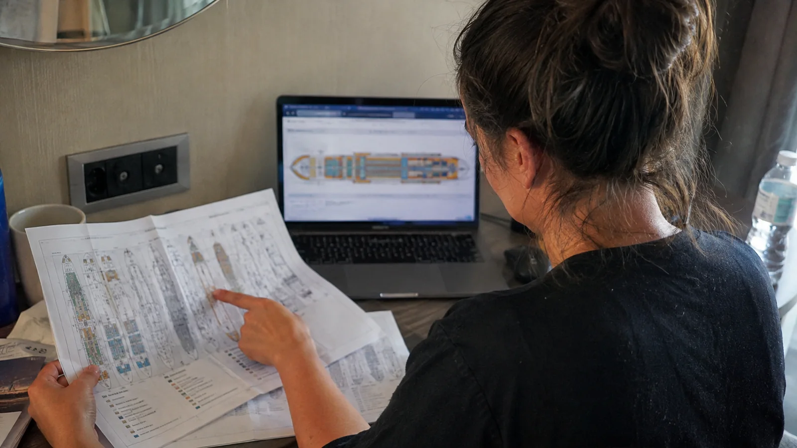 Woman pointing to a printed cruise ship deck plan beside a laptop