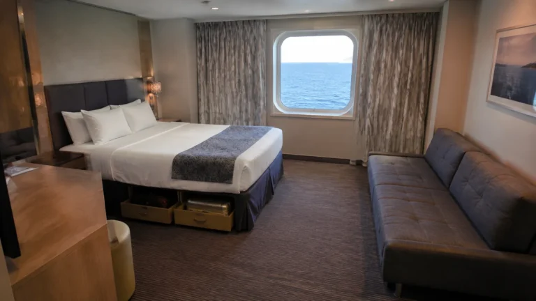 Cabin with a double bed, sofa, desk, and sea-view window.