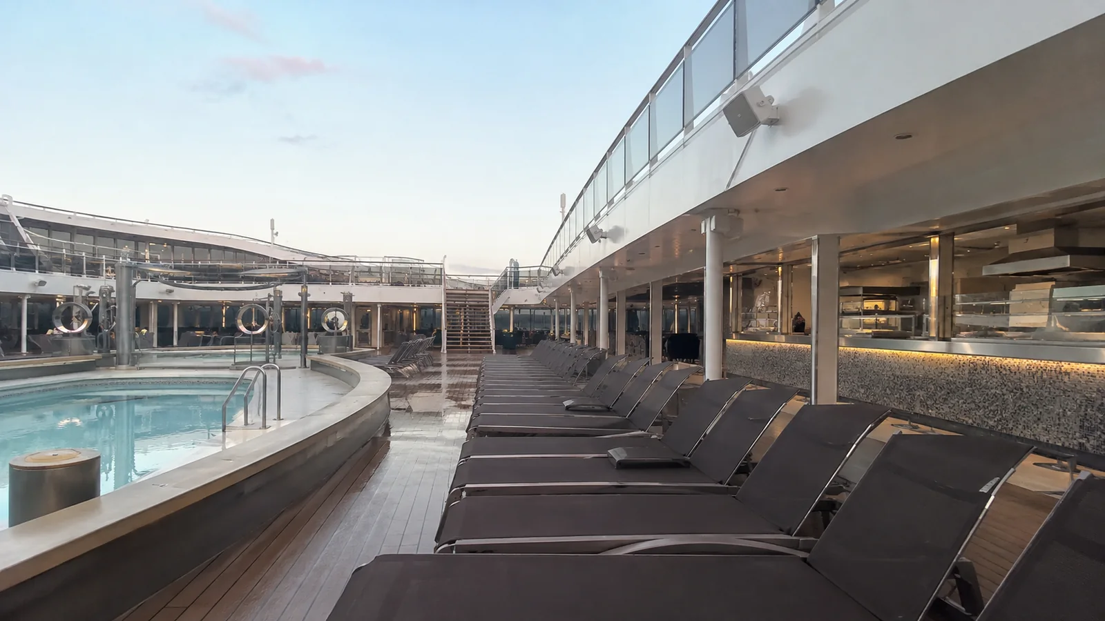 Empty loungers line a ship pool beside restaurant windows.