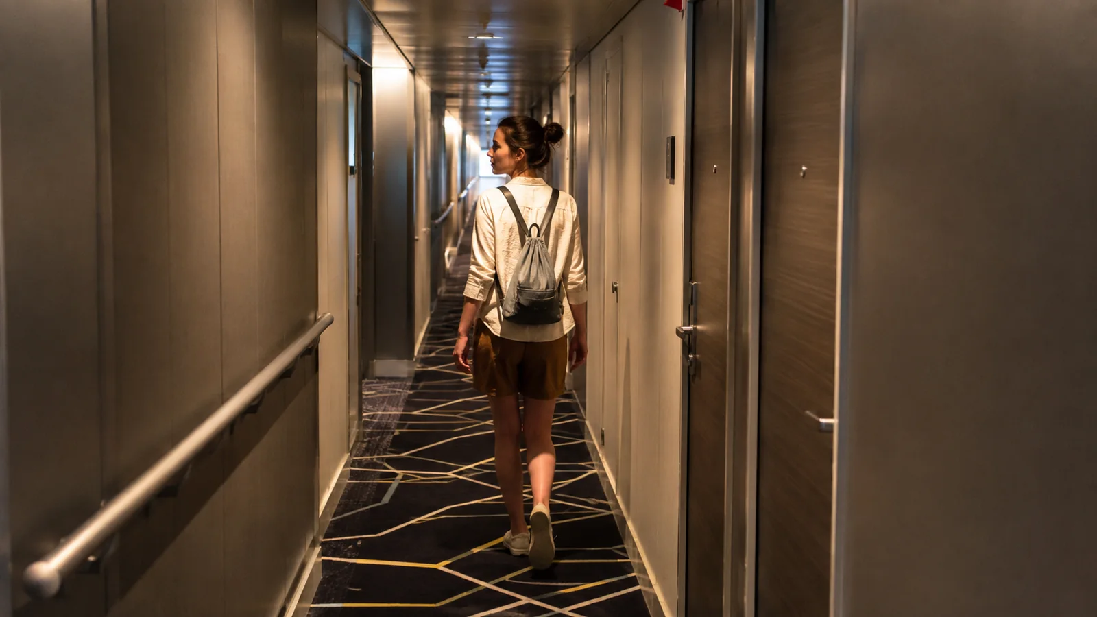 Woman walks through a softly lit corridor carrying a small bag.