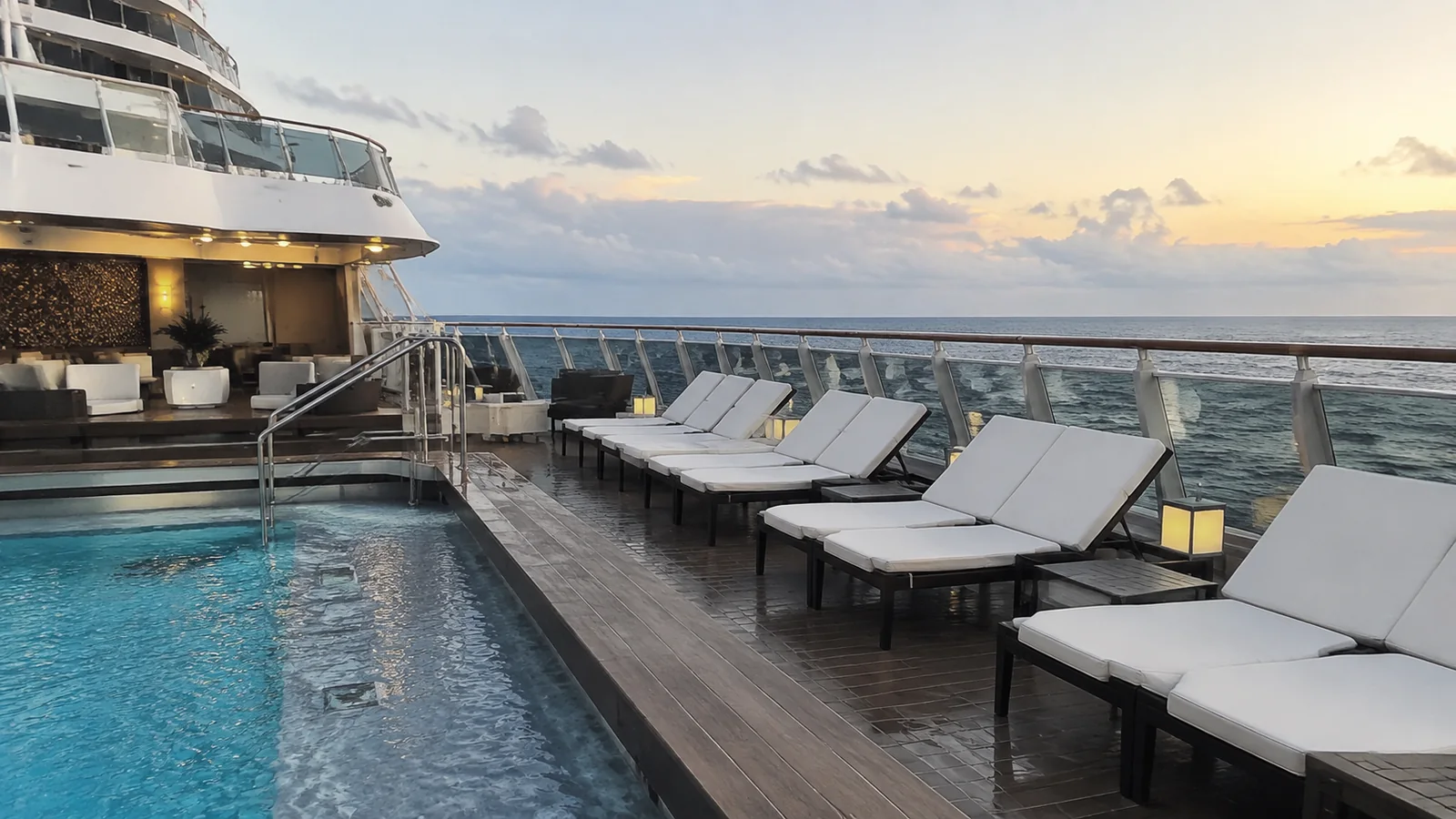 Empty cushioned loungers surround a small ship pool at sunset.