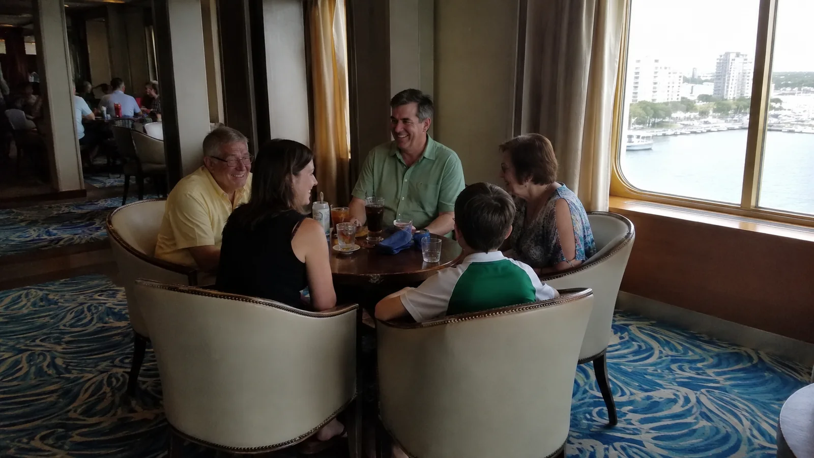 Family gathered around a table in an ocean-view ship lounge.