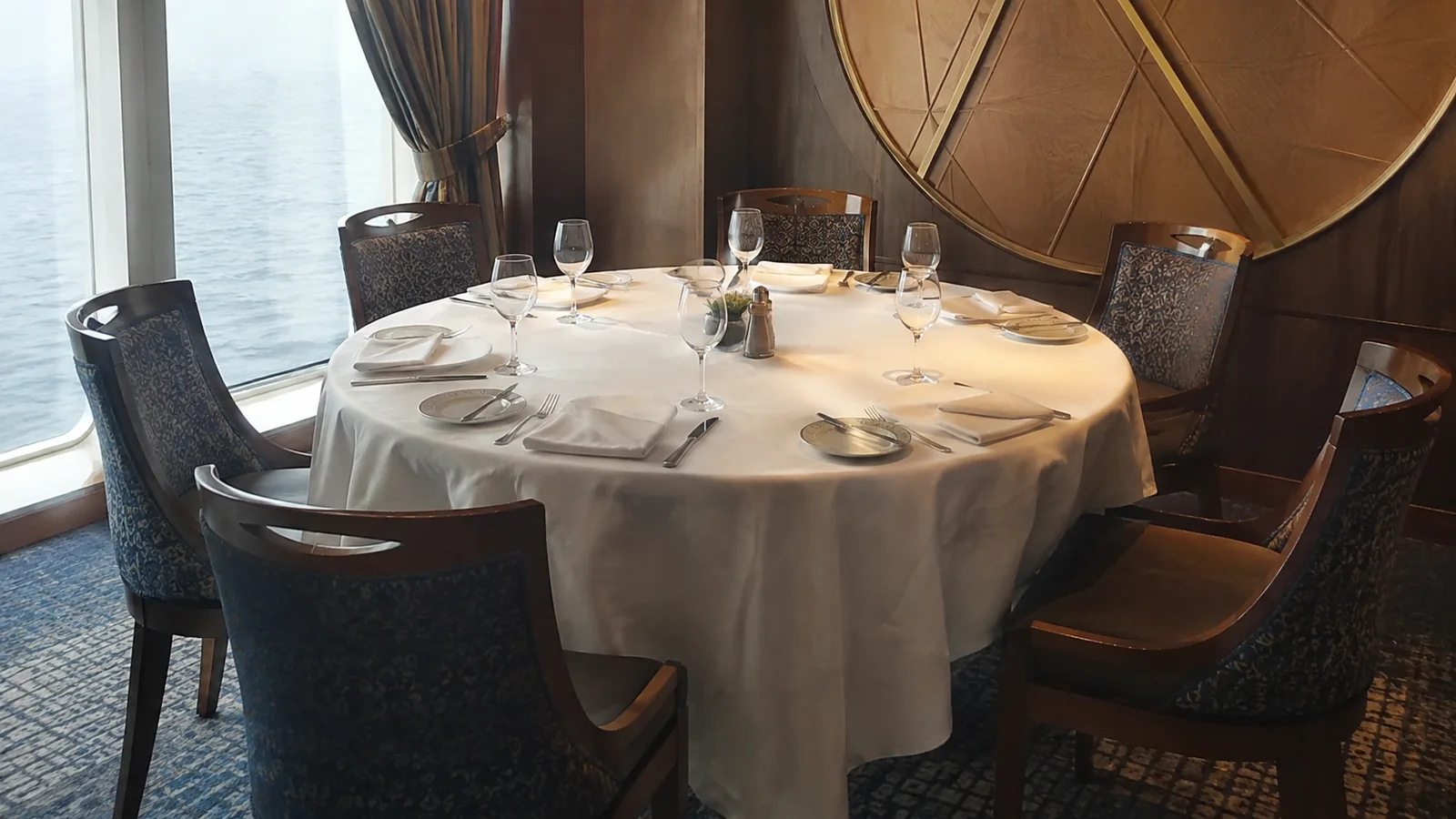 Round restaurant table set with white linens, plates, and wine glasses.
