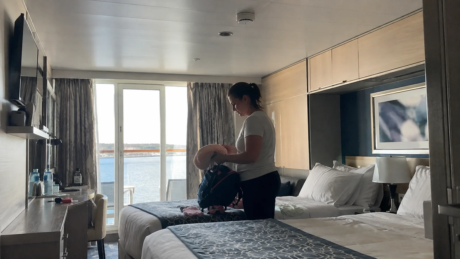 Woman packing a bag beside a cabin bed and balcony doors.