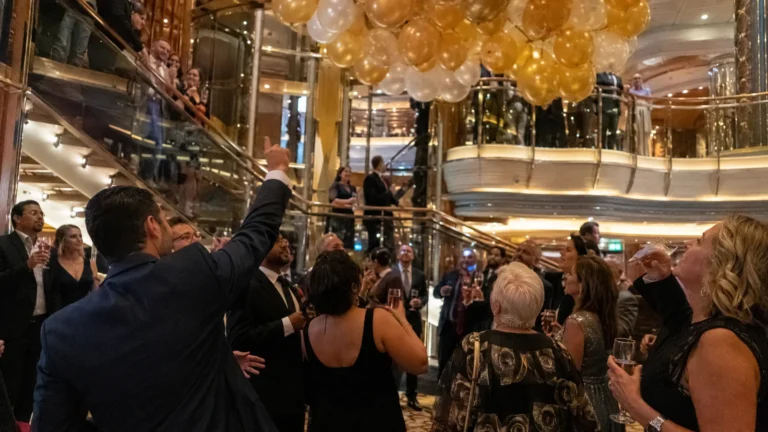 Passengers celebrating beneath gold and white balloons in a ship atrium.