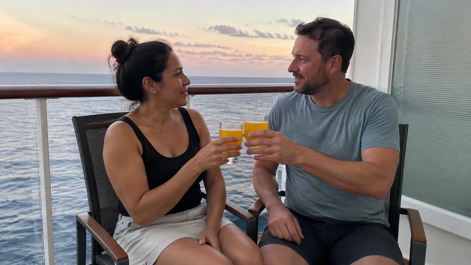Couple raising glasses together on a balcony at sunset.
