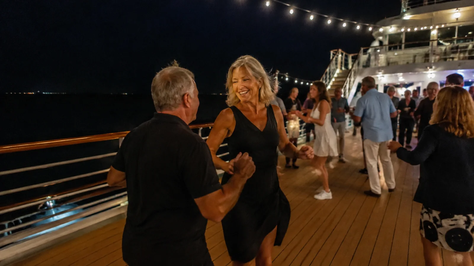 Couples dancing on a ship deck beneath string lights at night.