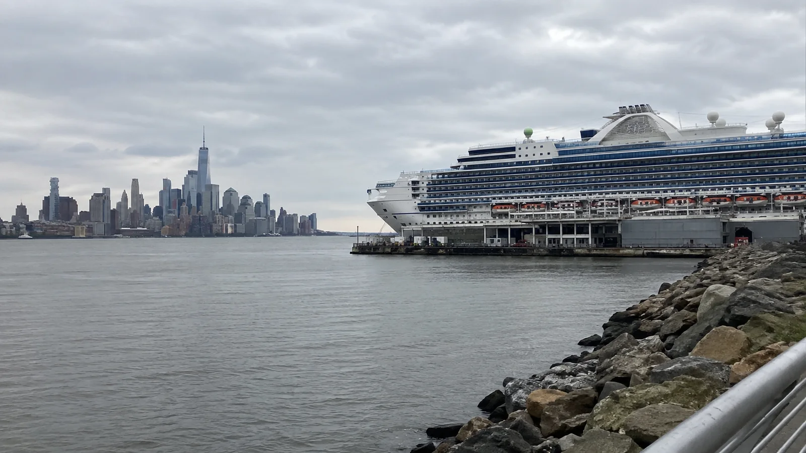 Cruise ship docked across the water with a city skyline behind it