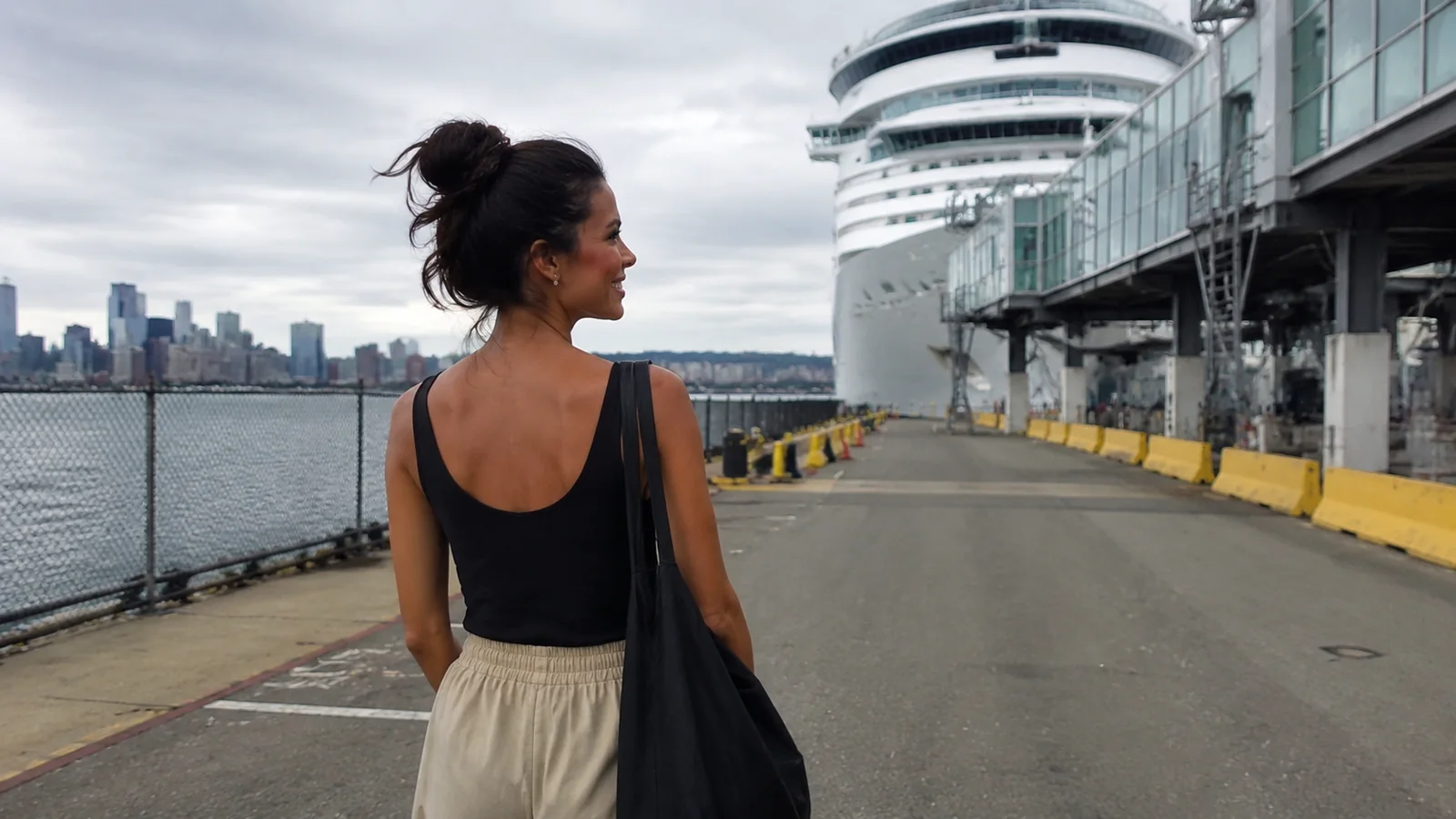 Woman standing on a pier with a cruise ship and city skyline behind her
