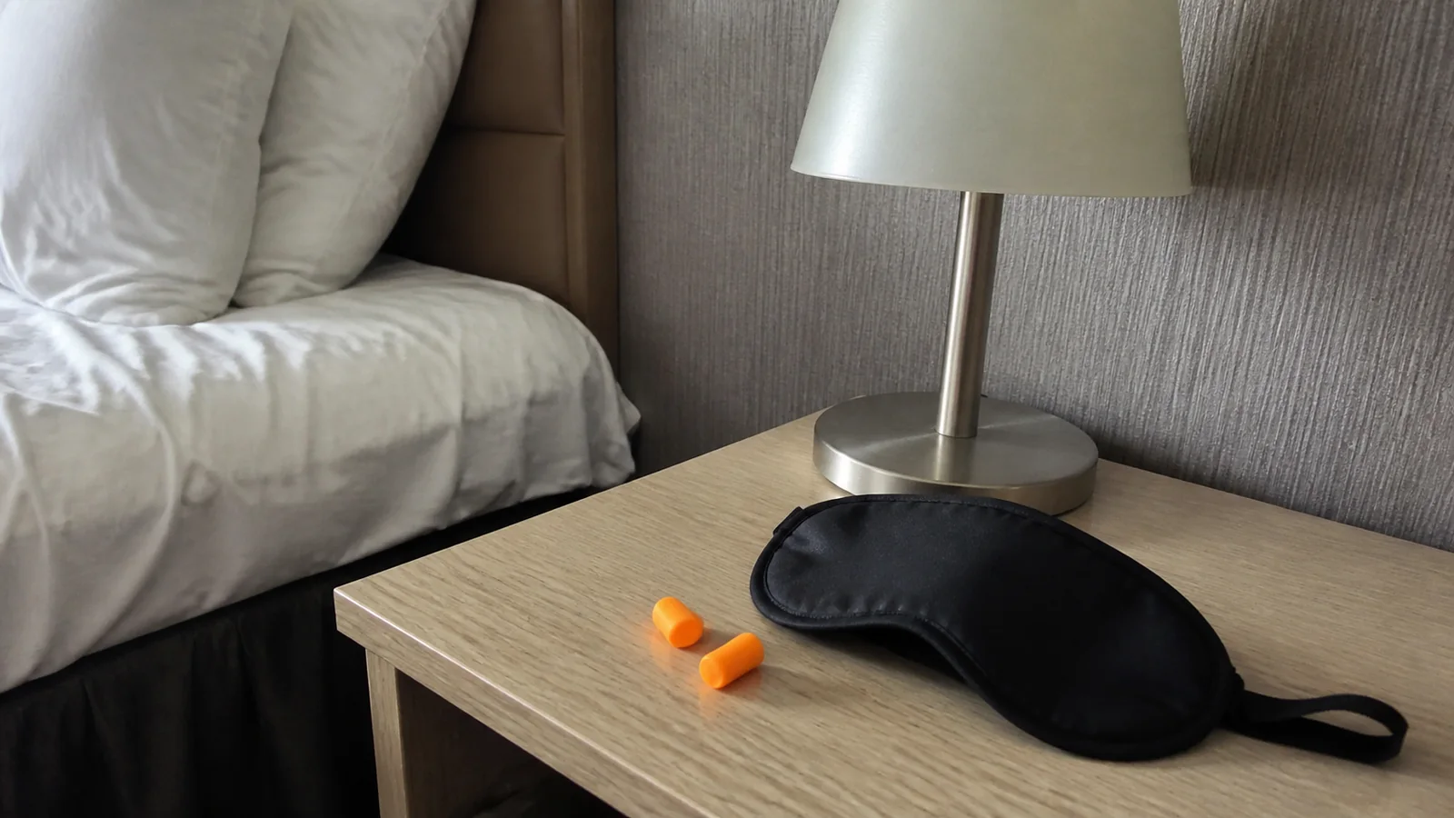 Sleep mask and orange earplugs on a bedside table.
