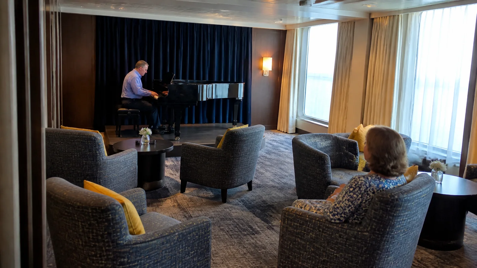 Passengers listening to a pianist in a small ship lounge.
