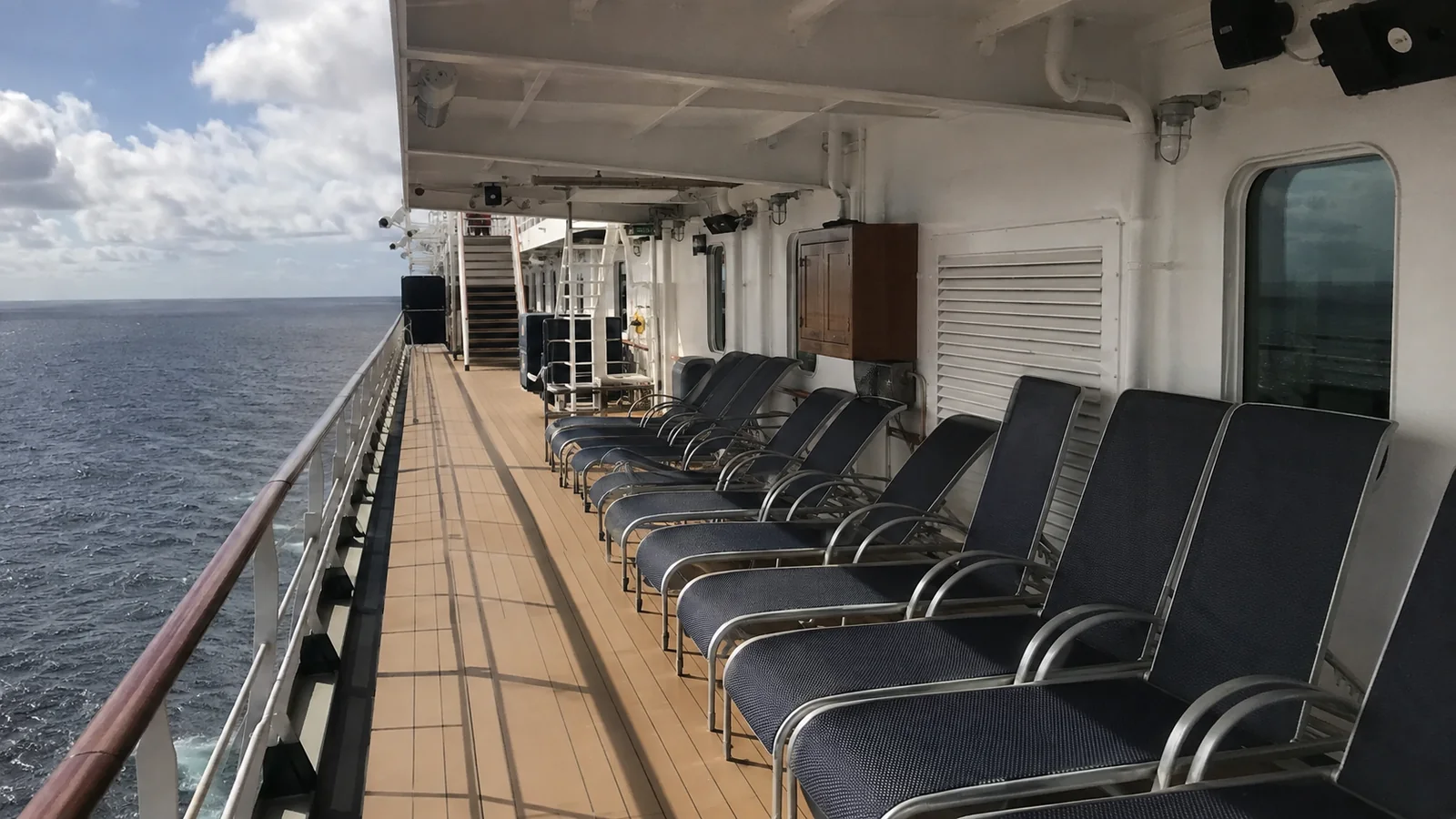Empty lounge chairs lining a cruise ship promenade above the ocean