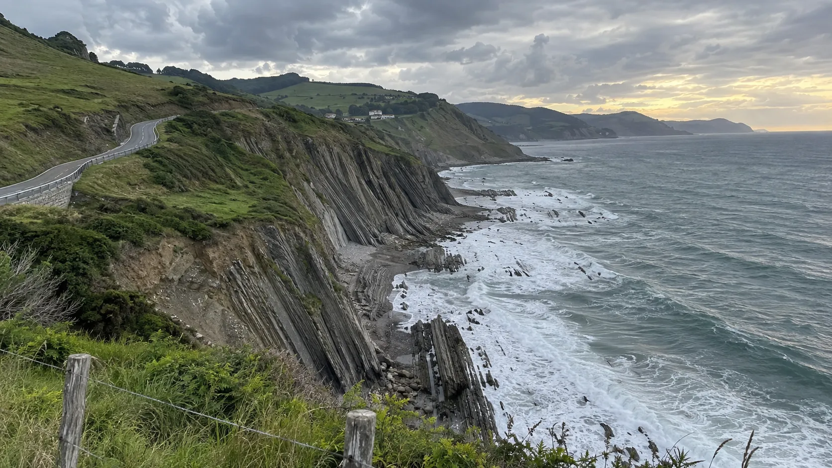 Coastal road curving above the folded flysch cliffs and surf near Zumaia in northern Spain.