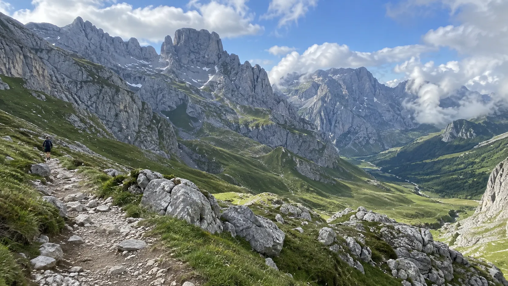 Hiker crossing an alpine trail beneath jagged limestone peaks in the Picos de Europa.