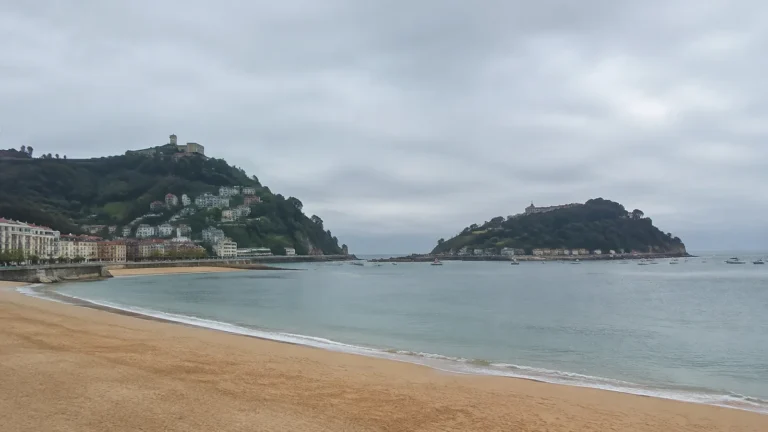 Curving sandy beach borders a sheltered bay between wooded headlands