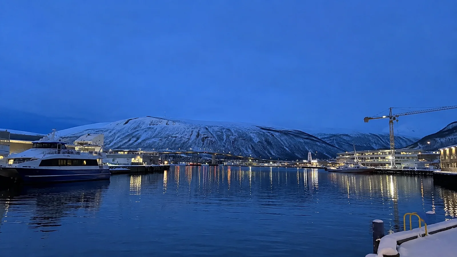 Snow-covered mountains behind an illuminated harbor at dusk