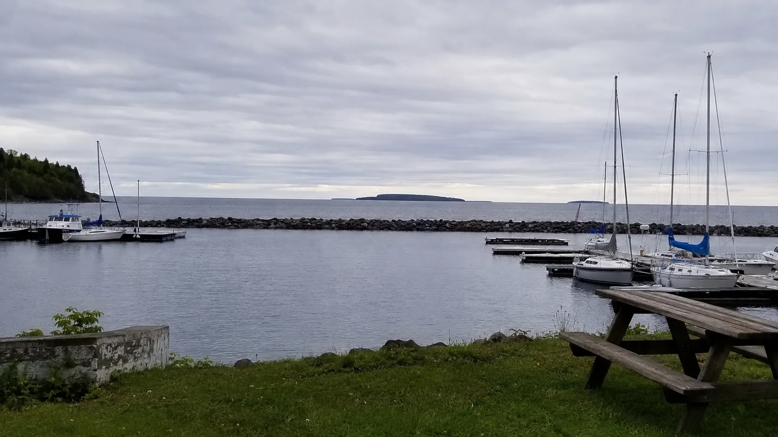 Quiet marina with sailboats and a picnic table beside the water.