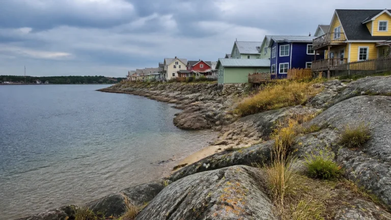 Colorful houses line a rocky shoreline beside clear shallow water.