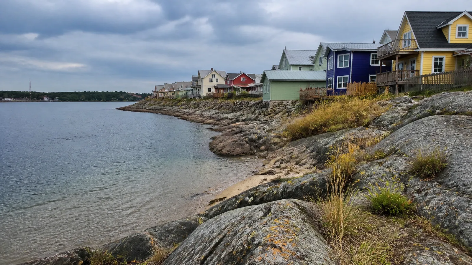 Colorful houses line a rocky shoreline beside clear shallow water.
