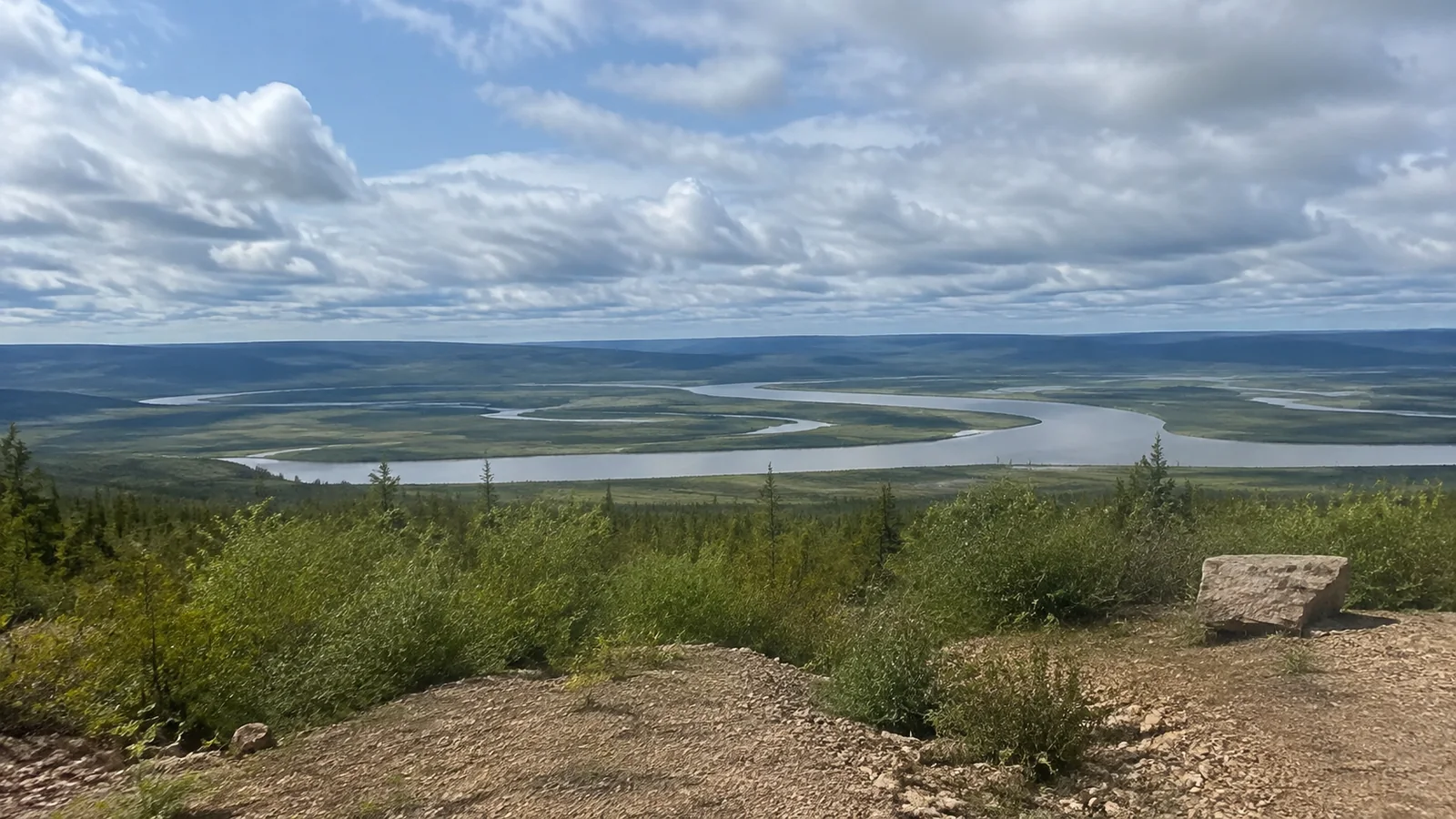 Broad winding river crosses a vast green valley under clouds.
