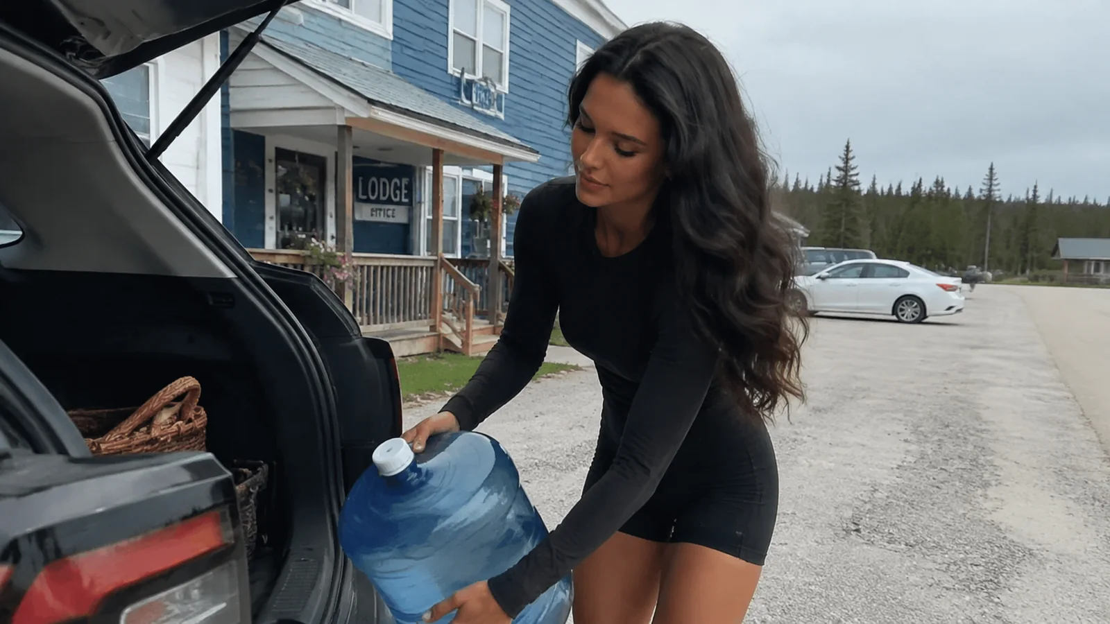 Woman loading a large water container into a car trunk.