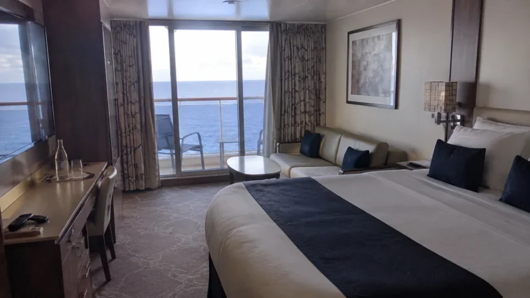 Cabin with a double bed, sofa, desk, and ocean-view balcony.